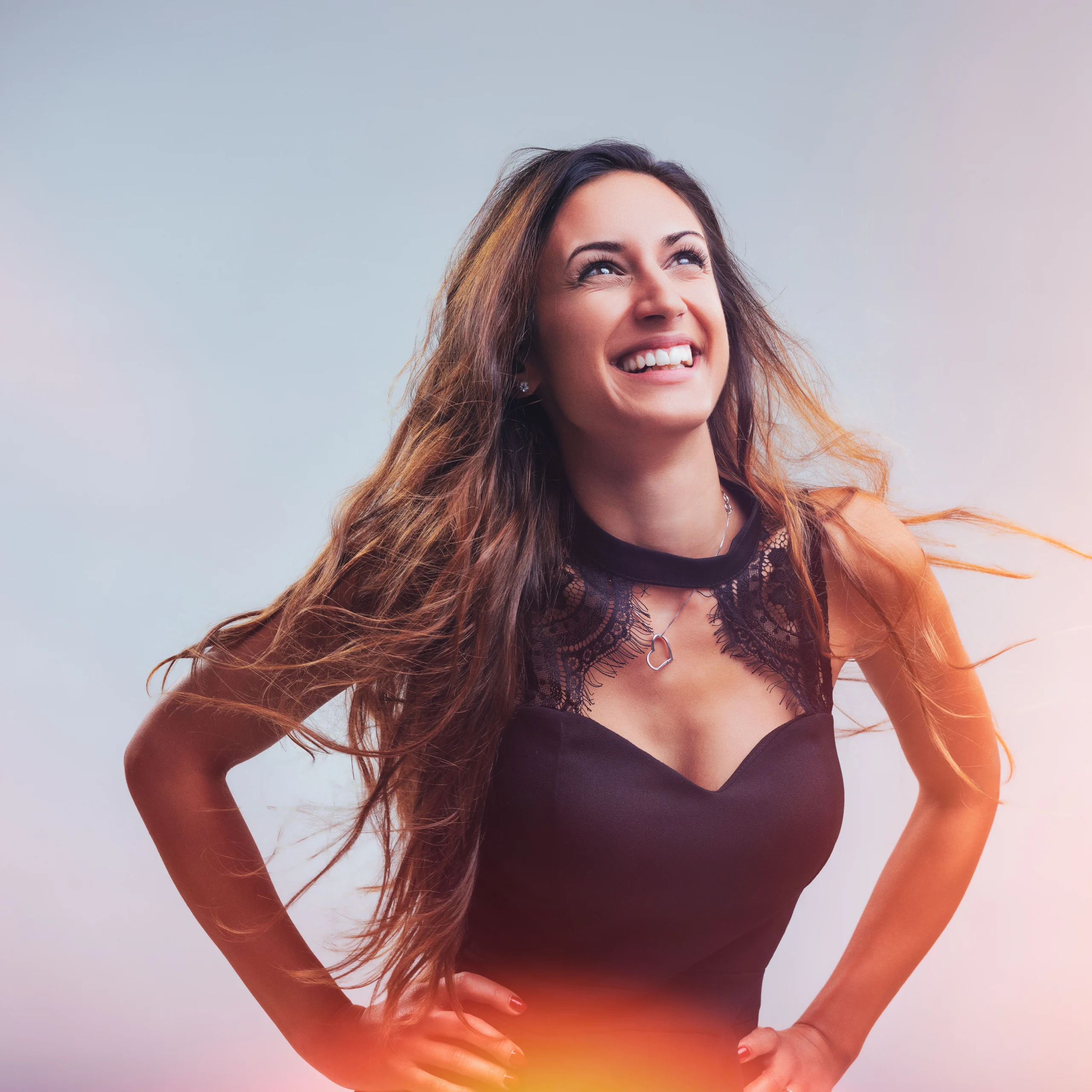A woman in a black lace dress smiles joyfully, her long hair flowing, with a dreamy, colorful lighting effect in the background.